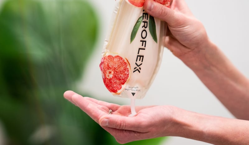A person gently squeezes an inverted AeroFlexx package to stream product directly into their palm, demonstrating a controlled and precise dispensing experience.